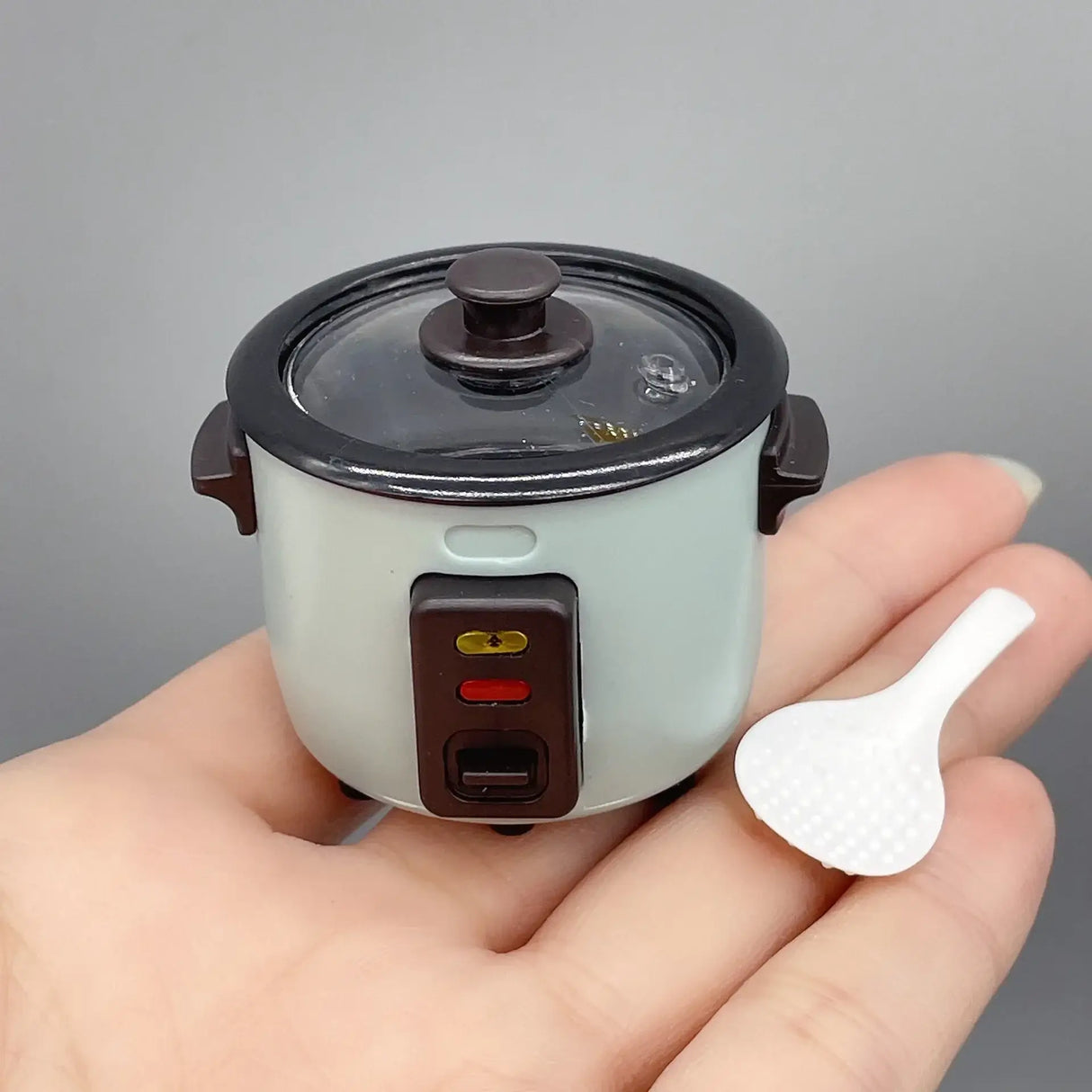 Miniature rice cooker prop in hand, ideal for photography or creative displays, showcasing intricate details and colors.