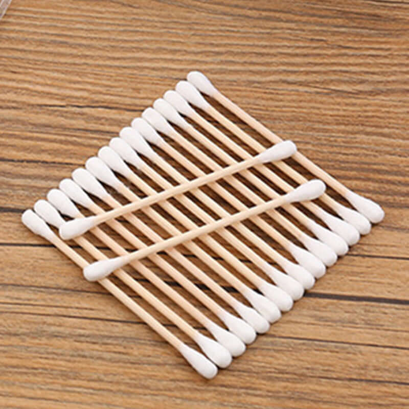 Baby cotton swabs made of wood with white cotton tips arranged neatly on a wooden surface.