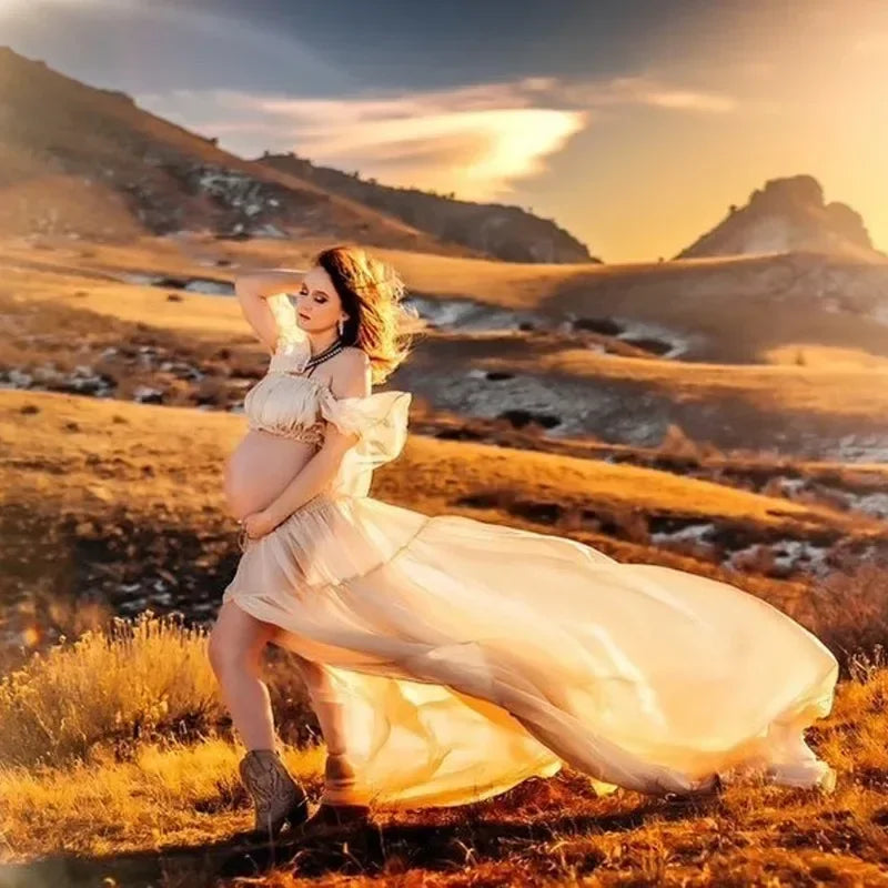 Pregnant woman wearing a flowy Boho maternity dress in a sunset landscape, ideal for baby shower photoshoots.