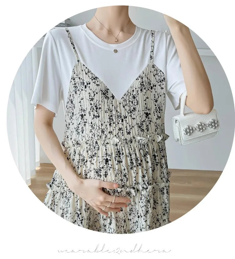Woman wearing an elegant mesh floral maternity dress with a white T-shirt, holding her baby bump. Perfect for baby showers.