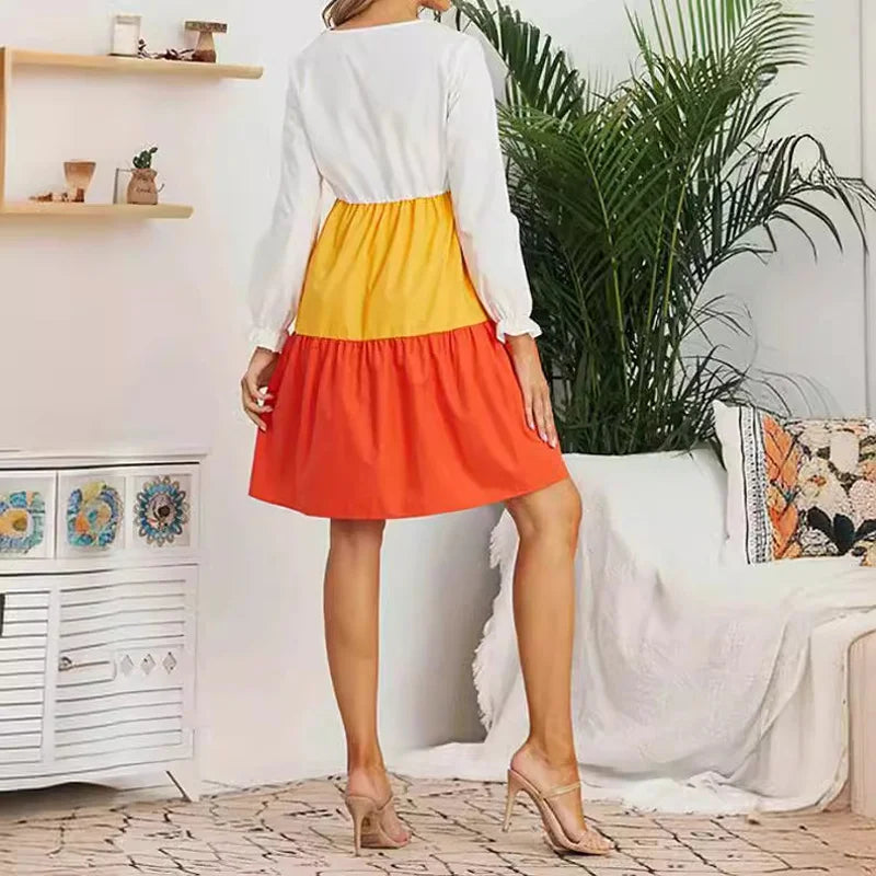 Back view of a woman wearing a V-neck color contrast maternity dress with long sleeves, featuring yellow and orange tiers.
