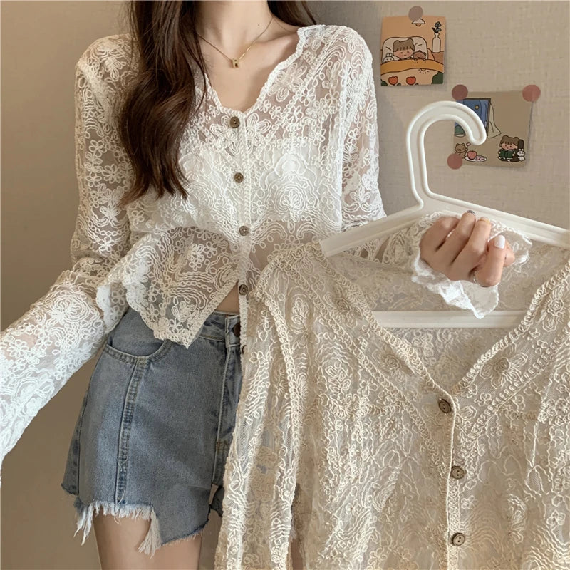 Woman holding a sheer lace sun shirt on a hanger, showcasing its intricate pattern and stylish design.