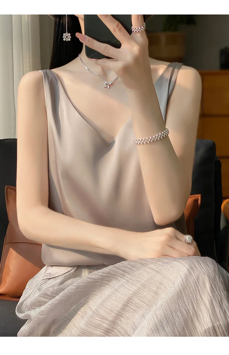 Woman wearing a stylish satin V-neck camisole with elegant jewelry, seated in a chic indoor setting.