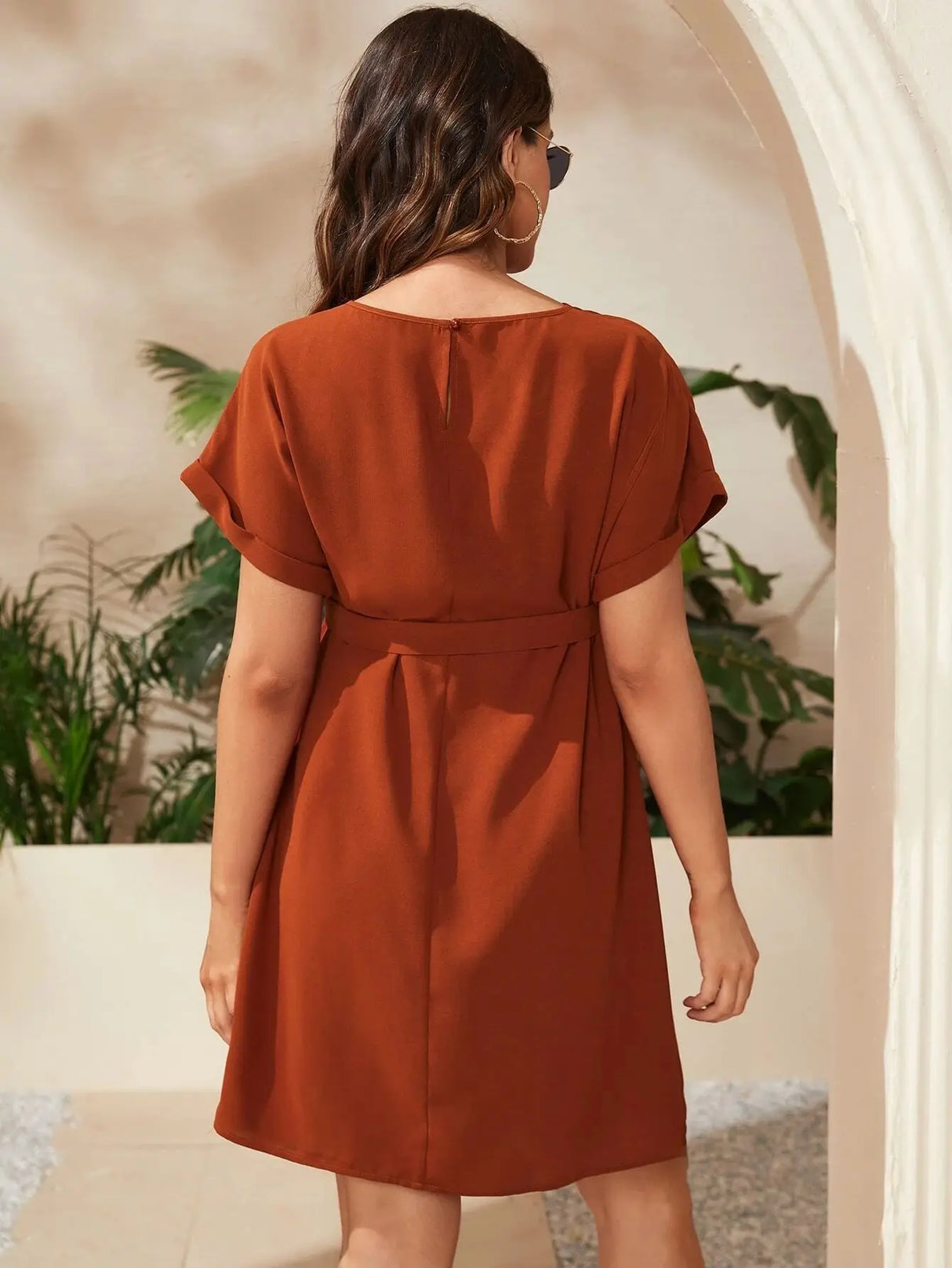 Back view of a woman in a brown bat-sleeve maternity tunic dress, showcasing its elegant knee-length design.