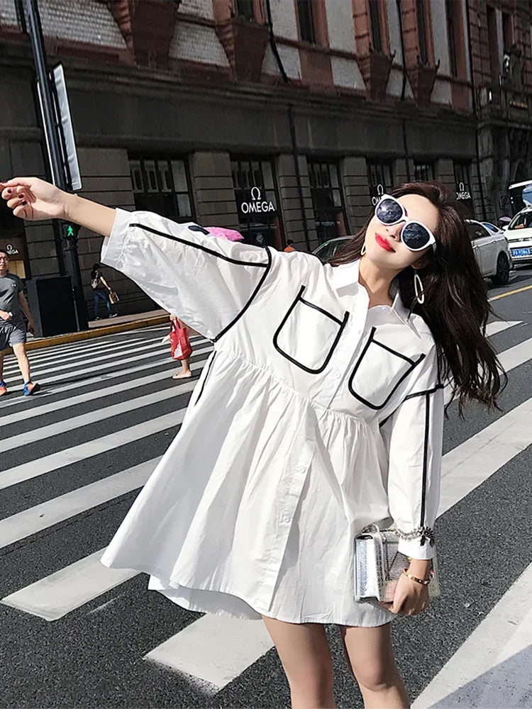 Stylish woman in a white maternity shirt dress with pockets, enjoying a sunny day on the street.
