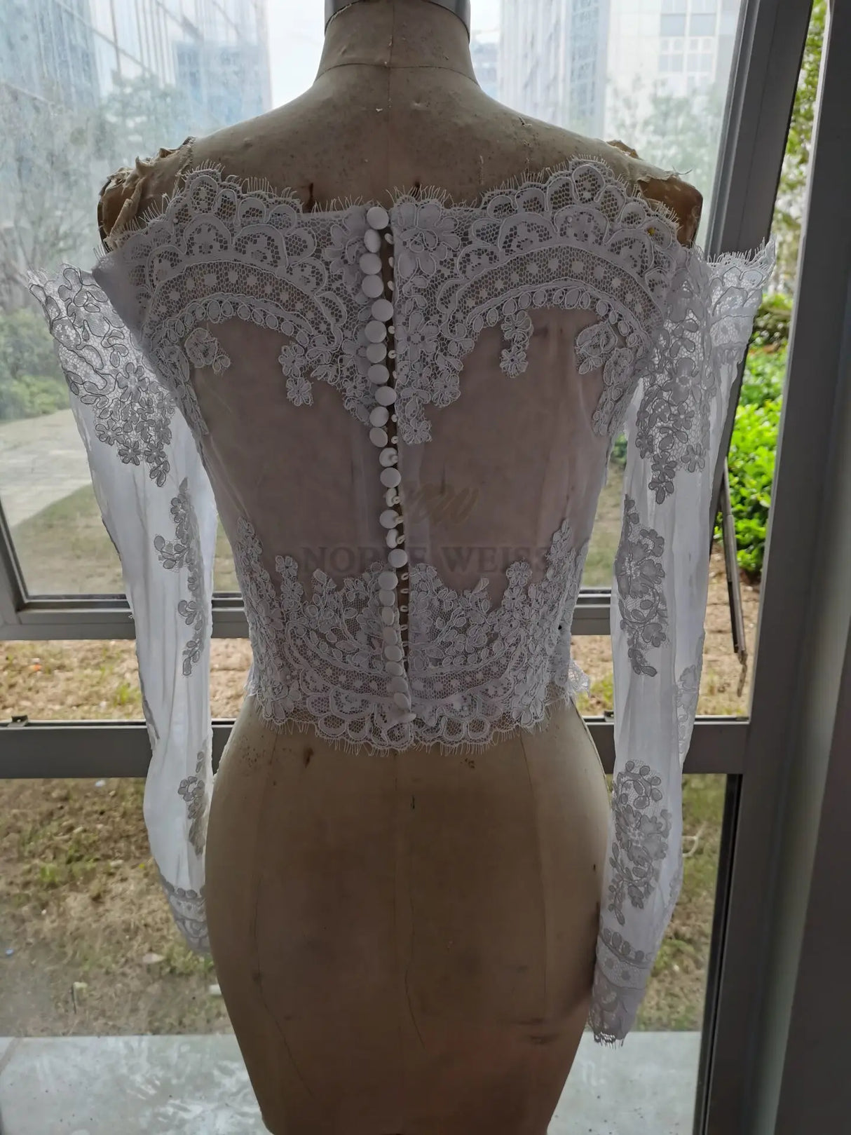 Lace off shoulder bridal jacket with long sleeves and detailed appliqué back design on dress form.