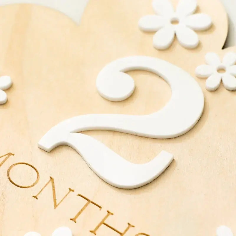 Close-up of a wooden milestone marker with the number 2 and decorative flowers, for tracking baby’s age in months.