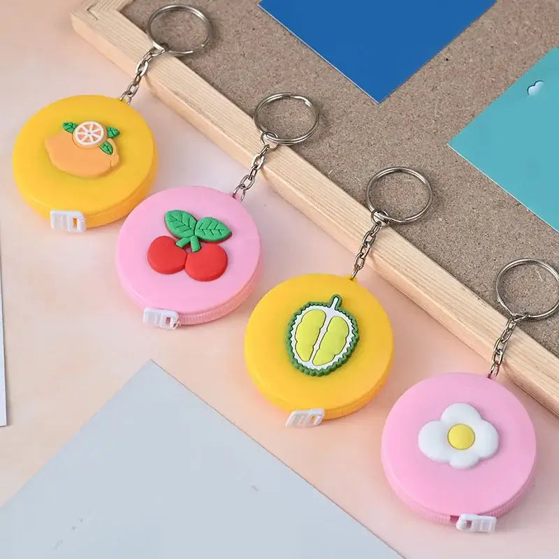 Assorted cute mini keychain tape measures with fruit designs in vibrant colors on a desk.
