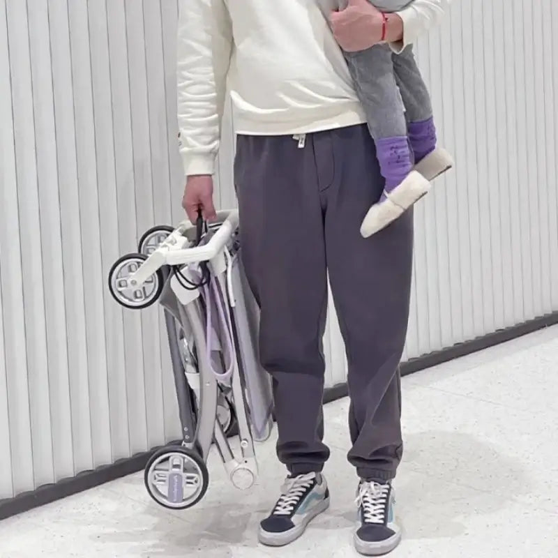 Parent holding a lightweight foldable children's stroller while carrying a child, showcasing travel convenience.