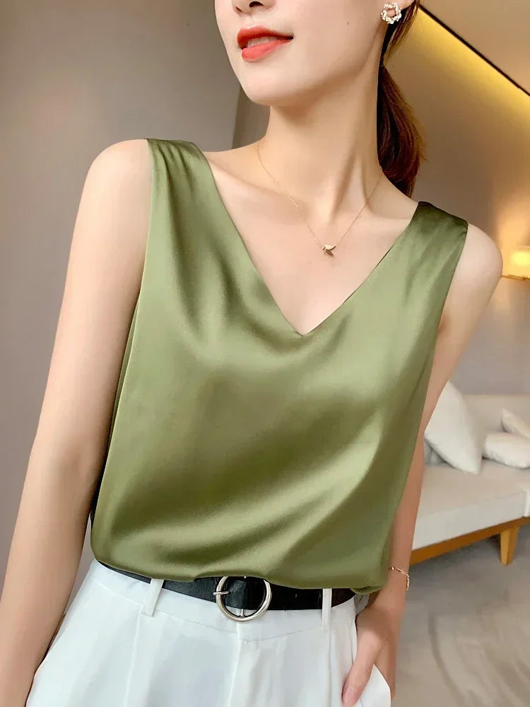 Woman wearing an elegant green satin V-neck camisole with a stylish belt and white trousers, showcasing summer fashion.