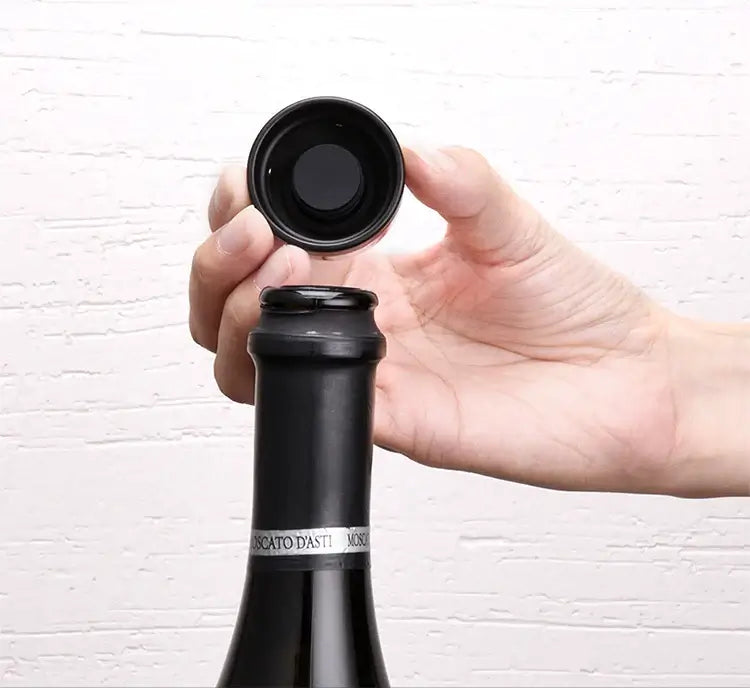Hand holding a silicone vacuum bottle cap stopper for sealing a red wine bottle, demonstrating its easy application.