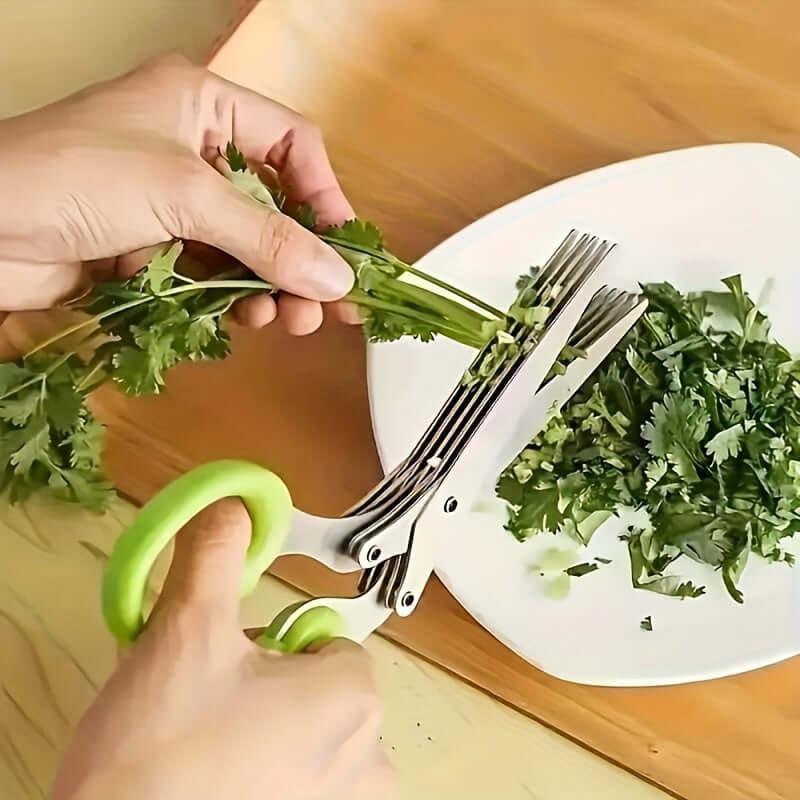 Person using durable stainless steel kitchen scissors to chop fresh cilantro on a wooden table.