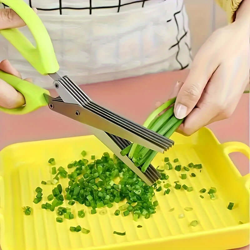 Durable stainless steel kitchen scissors cutting green onions on a yellow tray for food preparation.