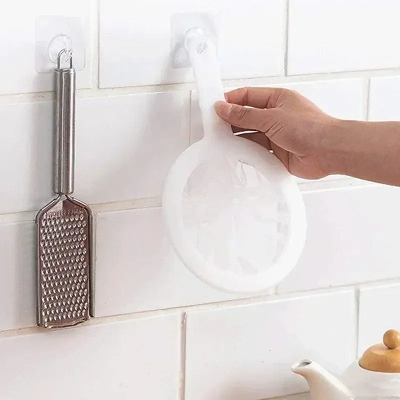 Hand using a white nylon strainer hanging on a kitchen wall next to a stainless steel grater, showcasing kitchen organization.