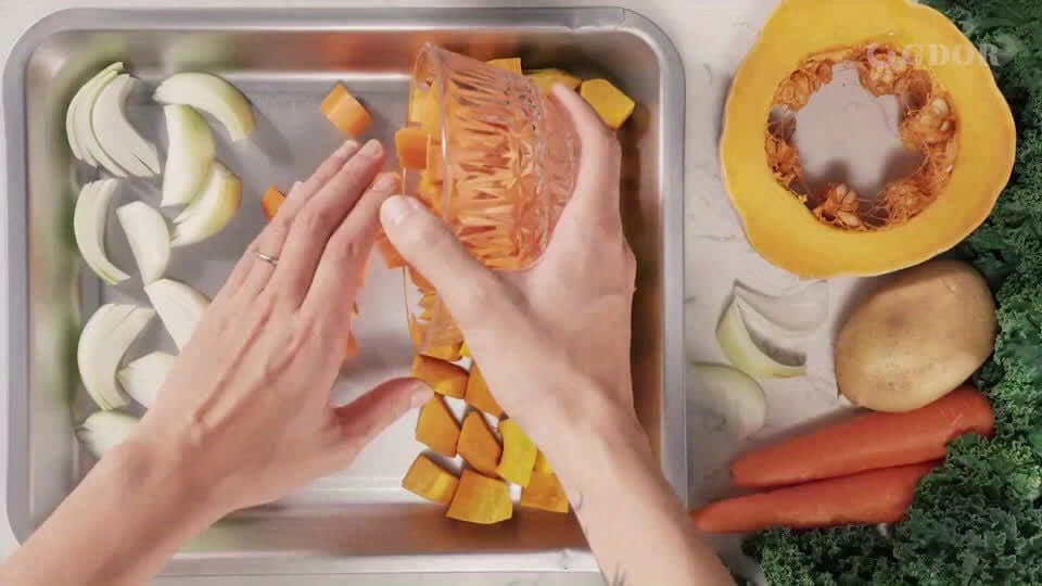 Hands preparing vegetables on a tray with a mix of chopped squashes, carrots, and onions for cooking.
