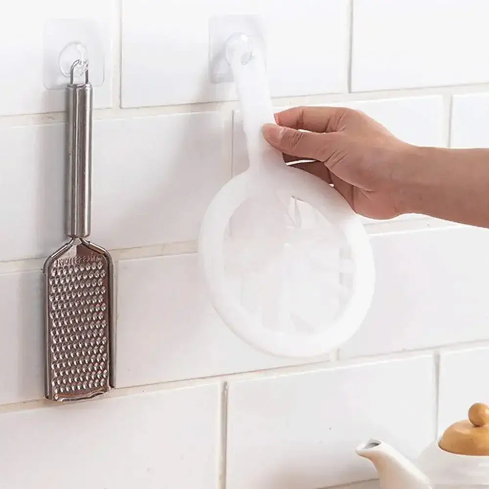 Hand holding a white nylon filter mesh strainer, alongside a metal grater on a kitchen wall.