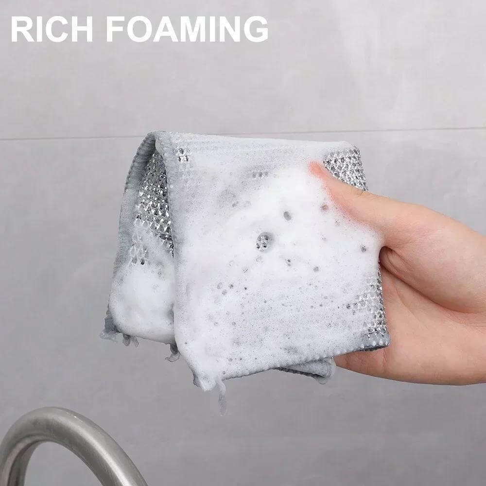 Person holding a gray dishwashing cloth covered in rich foam, demonstrating its cleaning power.