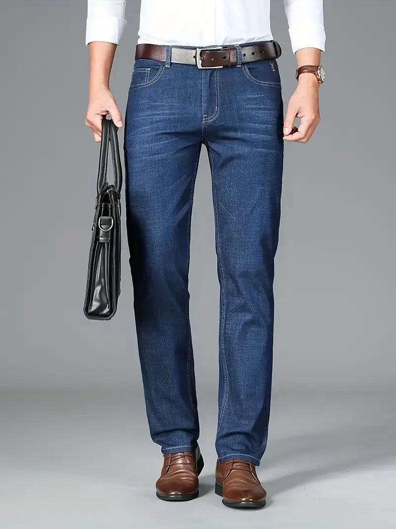 Stylish man wearing dark blue men's jeans with a white shirt and brown shoes, holding a black bag.