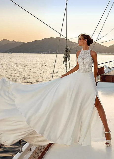 Elegant beach satin halter wedding dress with lace appliques and thigh-high slit, flowing gracefully at sunset.