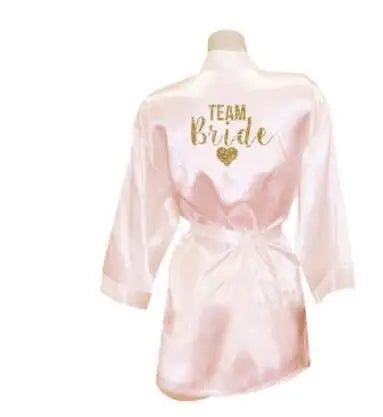 Light pink satin robe with 'Team Bride' text in gold glitter, perfect for bridesmaids and wedding celebrations.