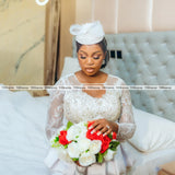 Bridal model wearing an African lace wedding dress with a crystal beaded design, holding a bouquet of red and white flowers.