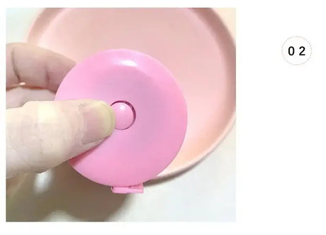 Close-up of a hand holding a pink mini height ruler next to a round pink plate, showcasing its usability for measuring.