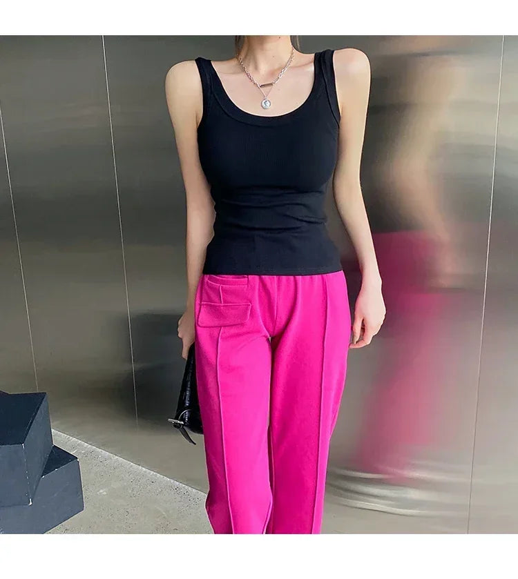 Model wearing a black sleeveless ribbed tank top paired with bright pink pants in a modern setting.