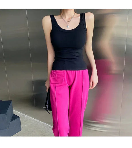 Model wearing a black sleeveless ribbed tank top paired with bright pink pants in a modern setting.