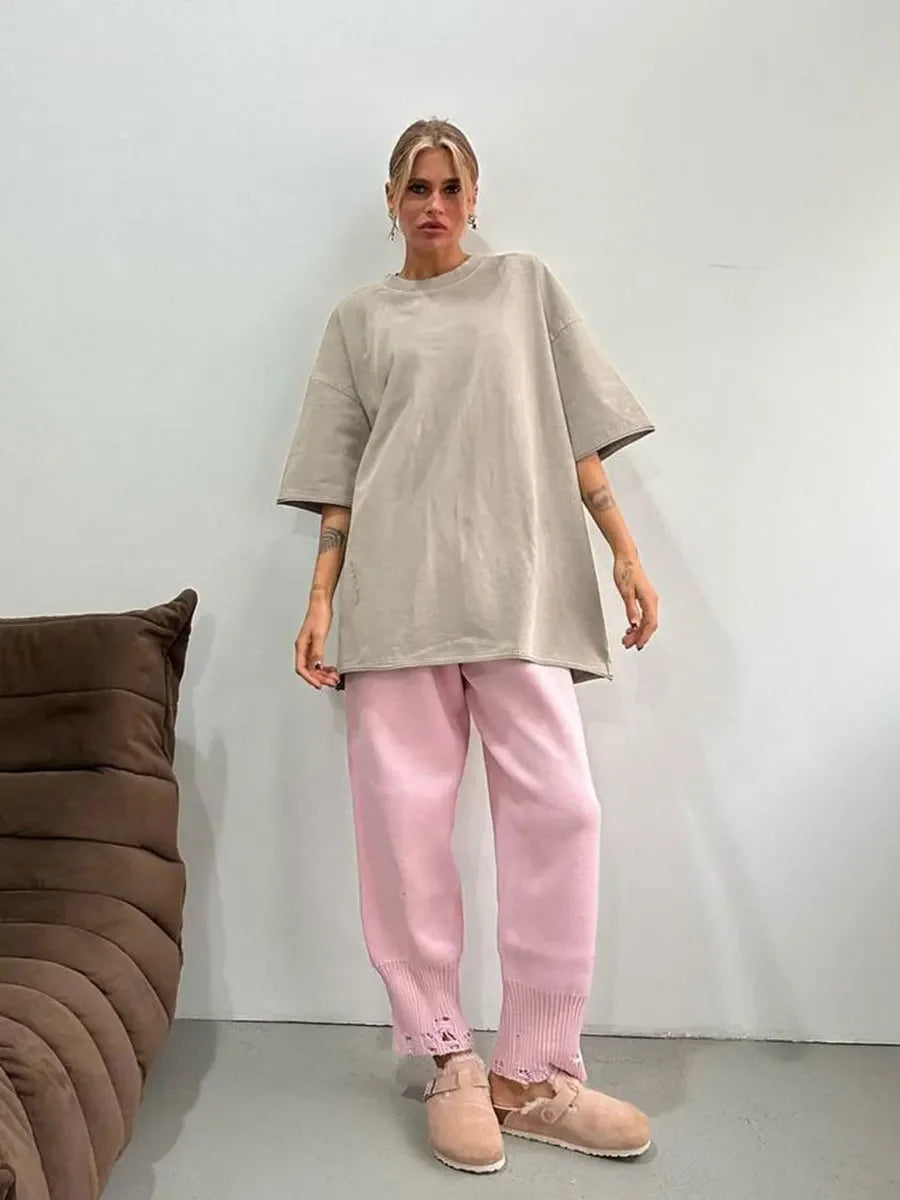 Woman wearing a loose, oversized beige T-shirt with pink knitted pants, standing in a casual setting.