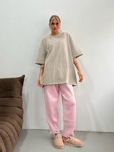 Woman wearing a loose, oversized beige T-shirt with pink knitted pants, standing in a casual setting.