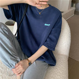 Oversized navy blue Harajuku streetwear tee featuring 'Newly' embroidery, styled casually with grey pants.
