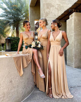 Three women wearing V-neck floor-length bridesmaid dresses in beige with floral bouquets, showcasing a stylish outdoor setting.