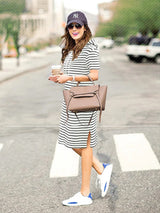 Woman in a striped maternity dress carrying a brown handbag, styled for summer with sneakers and a cap.