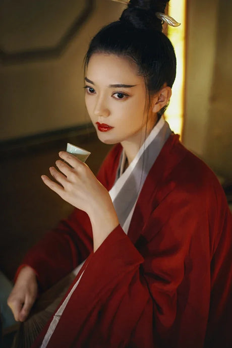 Woman in a wine red Hanfu costume holding a tea cup, showcasing Tang Dynasty elegance.