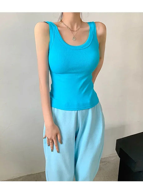Model wearing a sleeveless turquoise ribbed tank top with casual blue pants in a minimalistic setting.