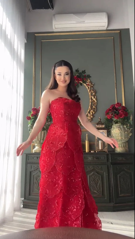 Model showcasing a stunning strapless red beaded gown with intricate lace details in an elegant indoor setting.