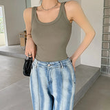 Woman wearing a sleeveless olive green ribbed tank top paired with light wash jeans in a stylish indoor setting.