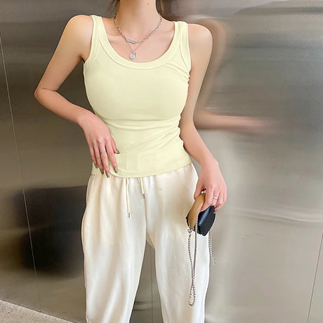 Model wearing a sleeveless yellow ribbed crop top paired with white pants, showcasing a trendy streetwear style.