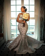 Elegant woman in a luxury mermaid wedding dress with beaded sheer sleeves, holding a bouquet by a window.