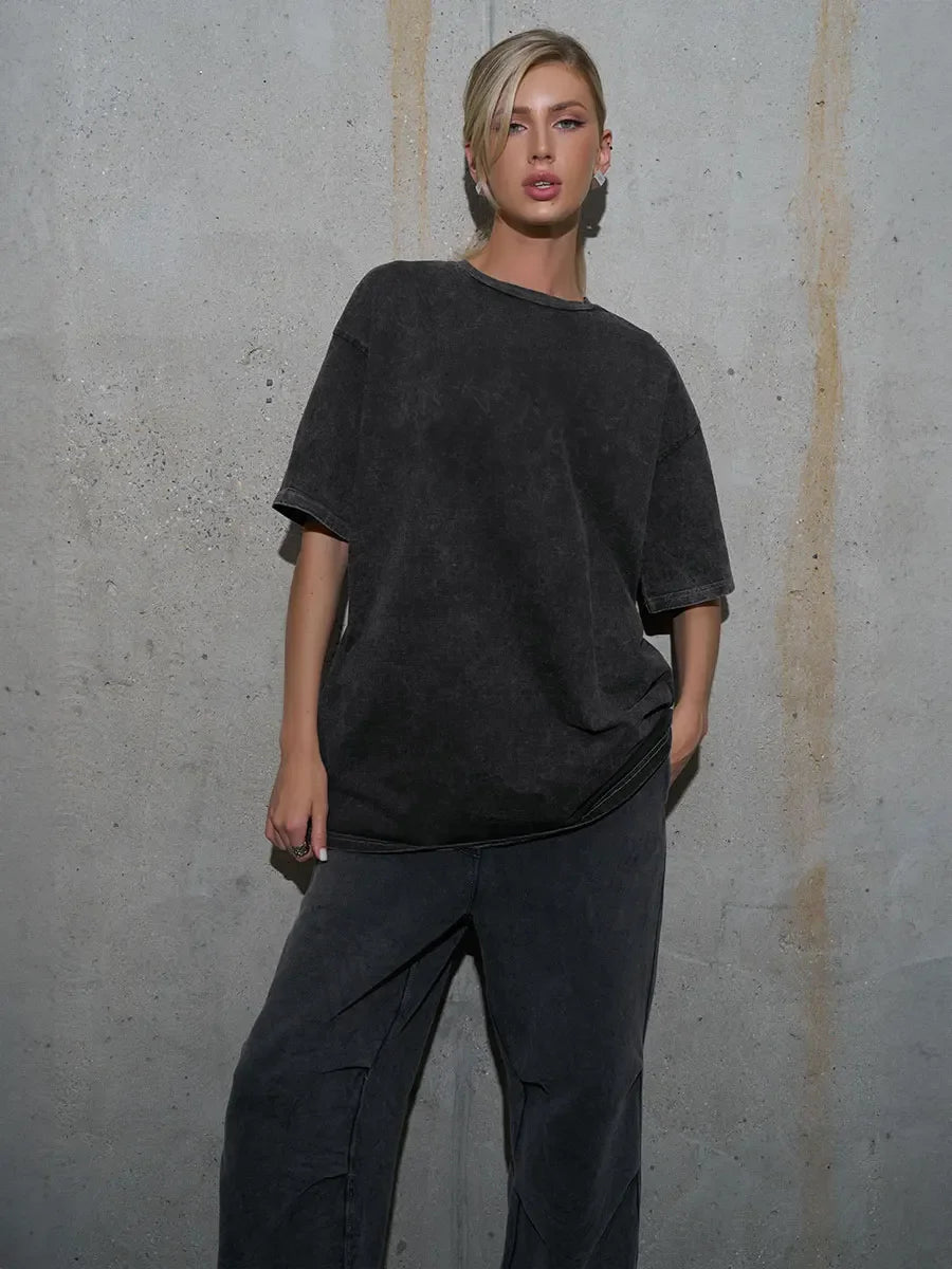 Woman wearing a loose-fit, dark casual t-shirt against a concrete wall, showcasing a trendy urban style.