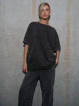Woman wearing a loose-fit, dark casual t-shirt against a concrete wall, showcasing a trendy urban style.