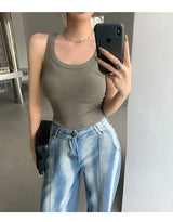Model wearing a sleeveless olive green ribbed tank top with blue jeans, showcasing casual streetwear style.