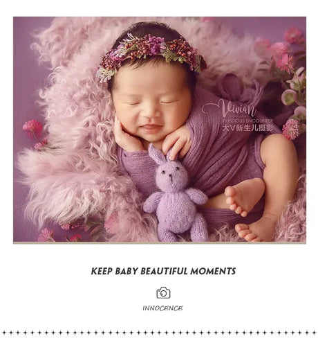 Newborn girl wearing a faux flower headband, smiling with a purple backdrop and soft textures, perfect for baby photography.