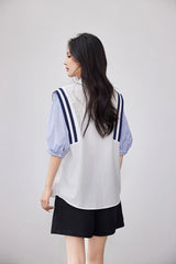 Back view of a woman wearing a colorblock chiffon shirt with striped sleeves and black shorts.