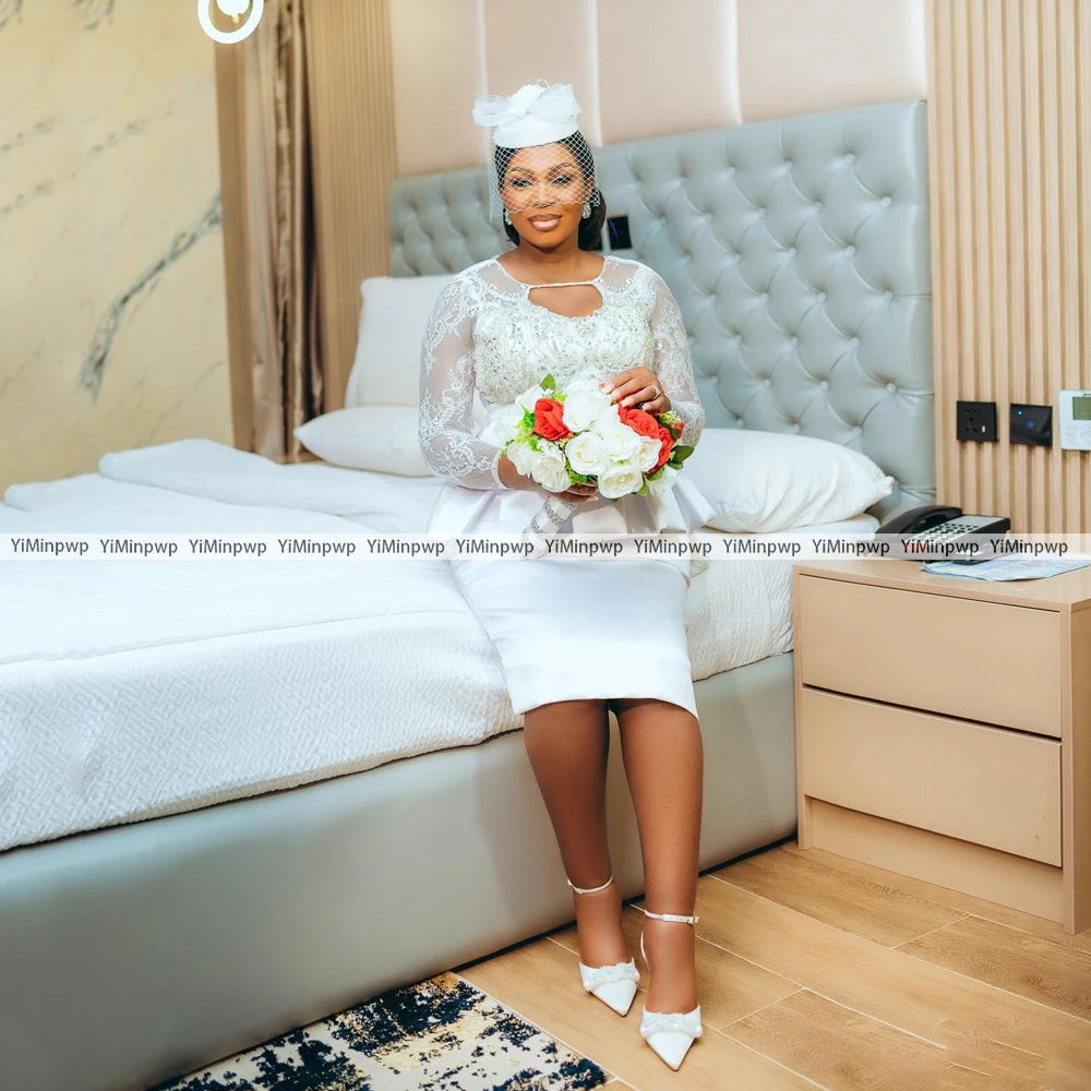 Bride wearing an African lace wedding dress with a bouquet, in a stylish bedroom setting.