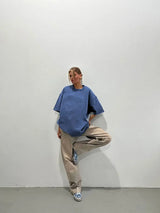 Woman wearing a loose-fitting blue casual t-shirt paired with beige pants, standing against a minimalist backdrop.