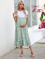 Pregnant woman in a floral green summer dress, showcasing comfortable maternity style for casual outings.