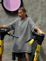 Woman wearing a loose gray casual t-shirt, posing with scooters against a textured background.