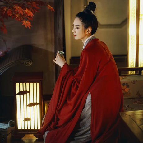 Elegant woman in red Swordsman Hanfu costume seated by lantern, showcasing Tang Dynasty style.