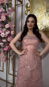 Pink beaded engagement gown with tiered skirt, worn by a model in front of floral decor.